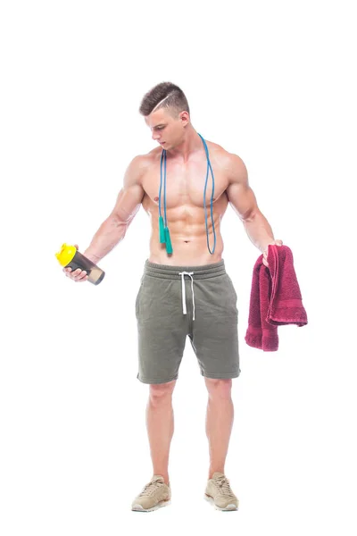 Gespierde man overslaan touw. Portret van gespierde jonge man met springen touw drinkwater met rode handdoek over de nek, geïsoleerd op witte achtergrond. Sterke atletische man-fitness model toont zijn — Stockfoto