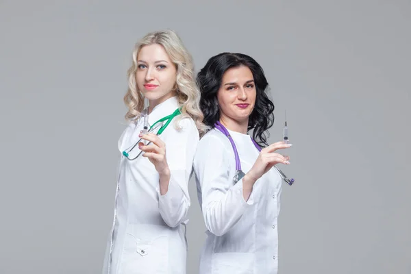 Две женщины-доктора стоят спиной к спине и держат шприцы для инъекций. — стоковое фото