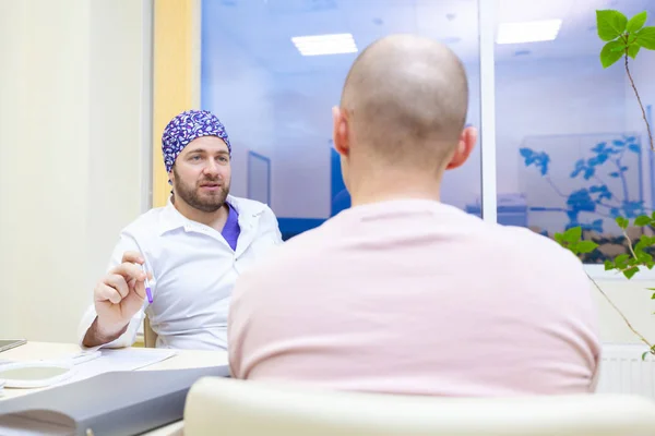 Baldness treatment. Patient suffering from hair loss in consultation with a doctor. Preparation for hair transplant surgery. The line marking the growth of hair. The patient controls the marking in