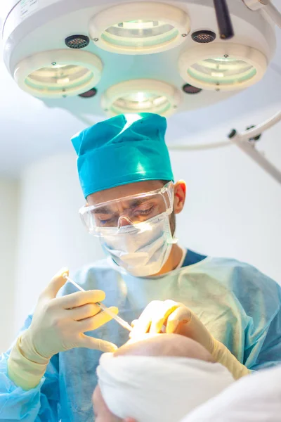 The surgeon gives injections to the head. Baldness treatment. Hair transplant. Surgeons in the operating room carry out hair transplant surgery. Surgical technique that moves hair follicles from a