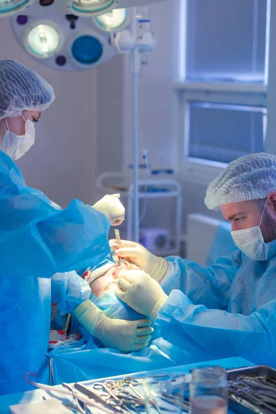 Surgeon and his assistant performing cosmetic surgery on nose in hospital operating room. Nose reshaping, augmentation. Rhinoplasty. Hammer. — Stock Photo, Image