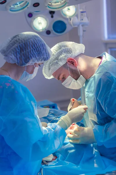 Surgeon and his assistant performing cosmetic surgery on nose in hospital operating room. Nose reshaping, augmentation. Rhinoplasty. Hammer. — Stock Photo, Image