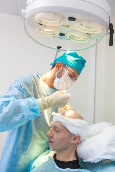 O cirurgião dá injeções na cabeça. Tratamento da calvície. Transplante de cabelo. Cirurgiões na sala de cirurgia realizar cirurgia de transplante de cabelo. Técnica cirúrgica que move os folículos pilosos de um — Fotografia de Stock