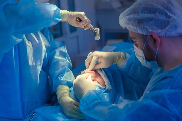 Surgeon and his assistant performing cosmetic surgery on nose in hospital operating room. Nose reshaping, augmentation. Rhinoplasty. Hammer. — Stock Photo, Image