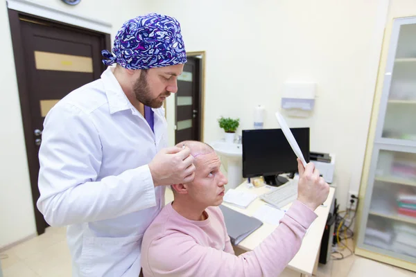 Baldness treatment. Patient suffering from hair loss in consultation with a doctor. Preparation for hair transplant surgery. The line marking the growth of hair. The patient controls the marking in — Stock Photo, Image