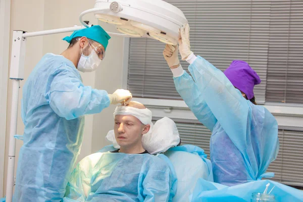 The surgeon directs the lamp light. Baldness treatment. Hair transplant. Surgeons in the operating room carry out hair transplant surgery. Surgical technique that moves hair follicles from a part of