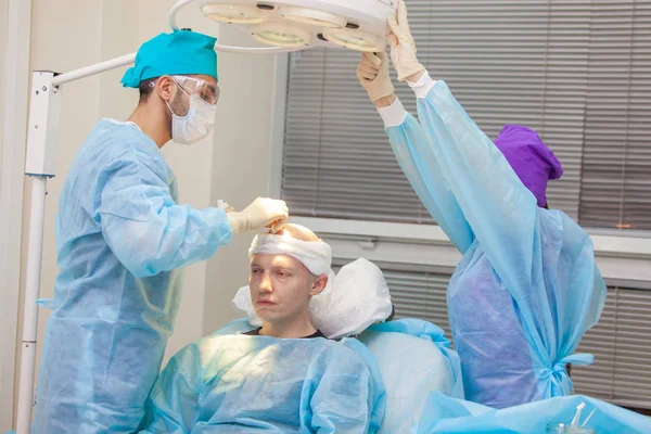 The surgeon directs the lamp light. Baldness treatment. Hair transplant. Surgeons in the operating room carry out hair transplant surgery. Surgical technique that moves hair follicles from a part of