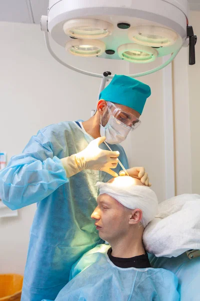 El cirujano le inyecta la cabeza. Tratamiento de la calvicie. Trasplante de cabello. Los cirujanos en el quirófano llevan a cabo una cirugía de trasplante de cabello. Técnica quirúrgica que mueve los folículos pilosos de un — Foto de Stock