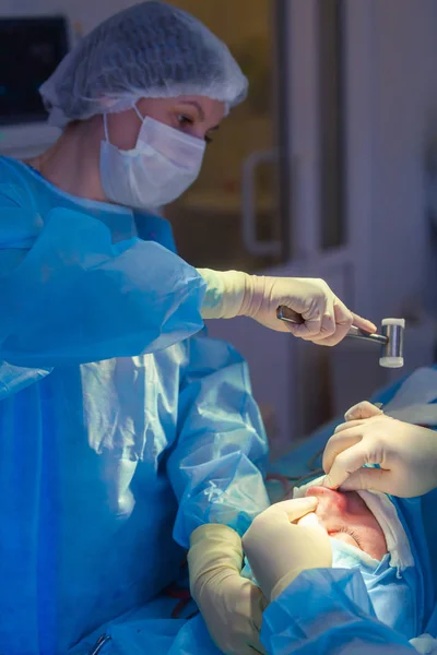 Dokter bedah dan asistennya melakukan bedah kosmetik pada hidung di ruang operasi rumah sakit. Hidung membentuk kembali, augmentasi. Rhinoplasty. Palu . — Stok Foto