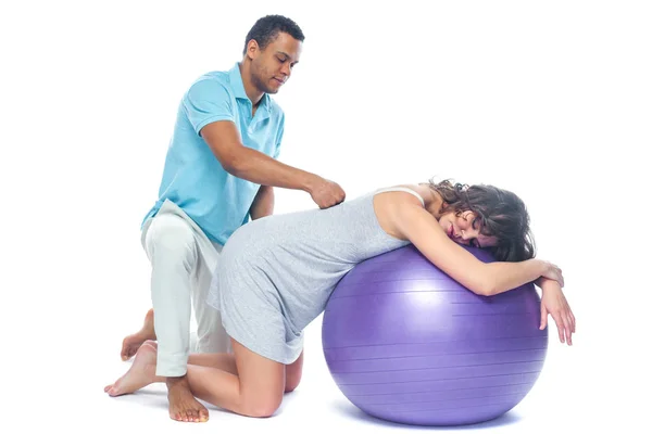 A young black man helps his white wife with birth pain with a ball. Partnered birth, partnered delivery. Isolated white background. — Stock Photo, Image