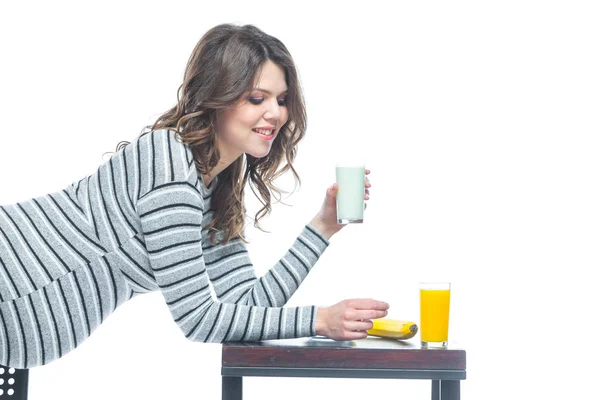 Une jeune femme enceinte s'assied à une table sur laquelle se trouve une banane, il y a une assiette avec des céréales, un verre avec du kéfir et du jus. Le concept de nutrition pendant la grossesse. Isolé sur fond blanc . — Photo