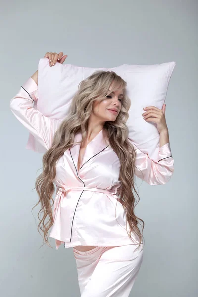 Young beautiful pregnant woman in pink pajamas with pink pillow. Lying on pillow. The concept of stylish pregnancy and beautiful sleep. On a gray uniform background. Copy paste.