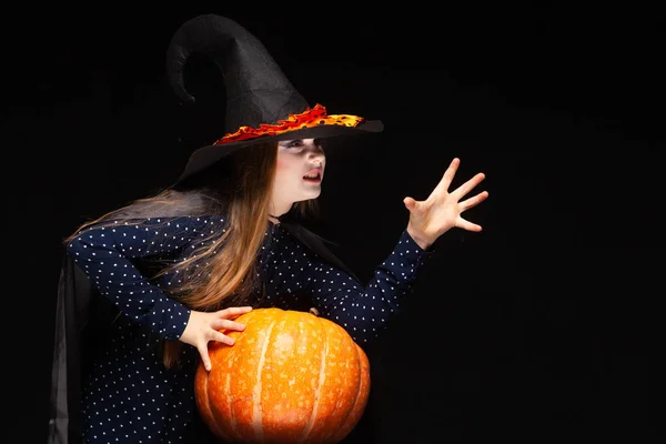 Halloween Witch with Pumpkin on black background Casts a spell with his hands. Beautiful young surprised woman in witches hat and costume holding pumpkin. Wide Halloween party art design. Copy-paste — Stock Photo, Image