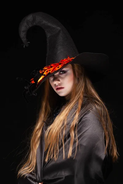 Halloween. Bruja con una araña en su sombrero sobre fondo negro. Hermosa joven sorprendida mujer en sombrero de brujas y la celebración del traje. Amplia fiesta de Halloween diseño de arte. Copia y pega. Concepto de bruja —  Fotos de Stock