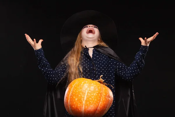 Halloween boszorkány sütőtök a fekete háttér nevet evilly. Gyönyörű fiatal meglepett nő boszorkányok kalap és jelmez gazdaságban. Széles Halloween Party Art Design. Copy-beillesztés. Witch Craft koncepció — Stock Fotó