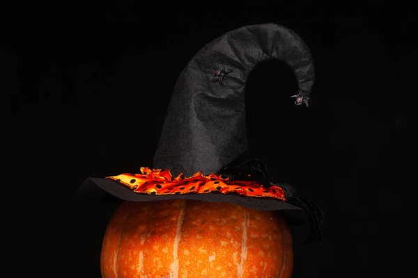 Halloween, celebration. Black witch hat with spiders on a beautiful big orange pumpkin. Design. The concept of the symbol of Halloween. Isolated black background.
