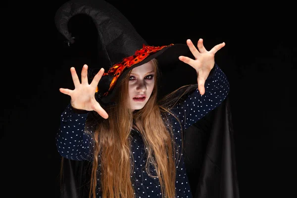 Halloween. Čarodějka s pavoukem na klobouku na černém pozadí vrhá zaklínadlo do rukou. Krásná mladá překvapená žena v čarodějové čepici a kostýmech. Široký Halloween umělecký design. Kopírovat — Stock fotografie