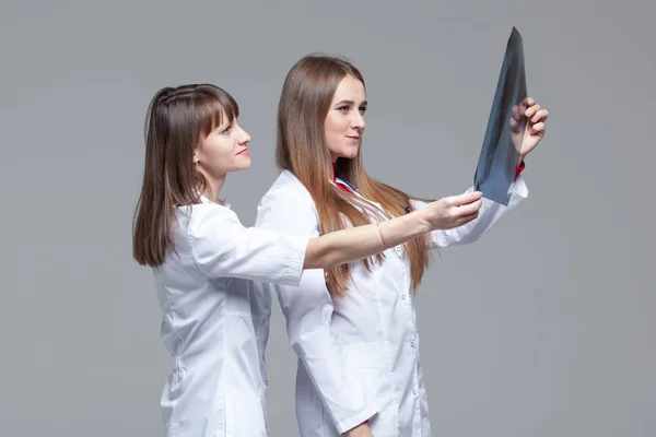 Dos doctores jóvenes mirando la imagen de rayos X de los pulmones sobre fondo gris —  Fotos de Stock