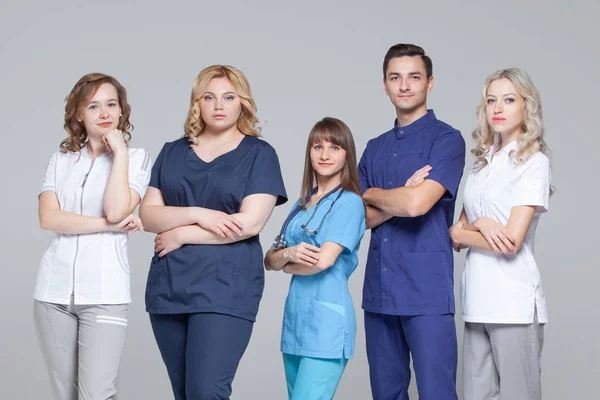 Успішна команда лікарів дивиться на камеру, стоячи на сірому фоні — стокове фото