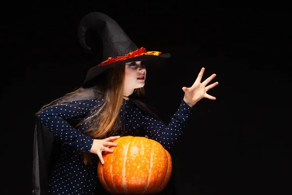 Halloween boszorkány sütőtök fekete háttérrel vet egy varázslatot a kezével. Gyönyörű fiatal meglepett nő boszorkányok kalap és jelmez gazdaság sütőtök. Széles Halloween Party Art Design. Másolás-beillesztés — Stock Fotó