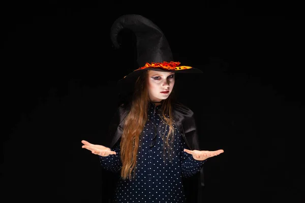 Sorcière d'Halloween sur fond noir. Belle jeune femme surprise en chapeau et costume de sorcières. Design d'art de fête Halloween large. Copier-coller. Le concept d'échelles, offre de choisir des cadeaux, placer des articles — Photo