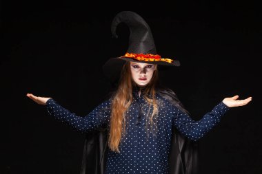 Siyah arka planda Cadılar Bayramı Cadısı. Cadılar şapka ve kostüm güzel genç sürpriz kadın. Geniş Cadılar Bayramı parti sanat tasarımı. Kopyala-yapıştır. Ölçekler kavramı, hediyeler seçmek için sunuyor, yer öğeleri