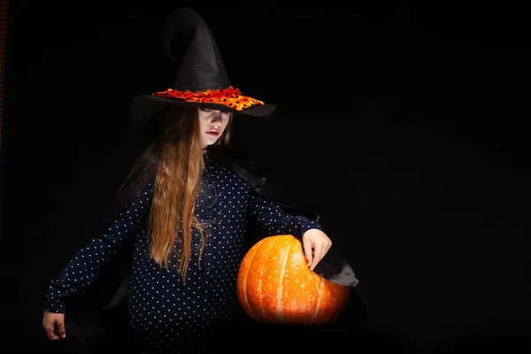 Bruja de Halloween con calabaza sobre fondo negro. Hermosa joven sorprendida mujer en sombrero de brujas y traje de calabaza celebración. Amplia fiesta de Halloween diseño de arte. Copia y pega. Concepto de bruja. Araña —  Fotos de Stock