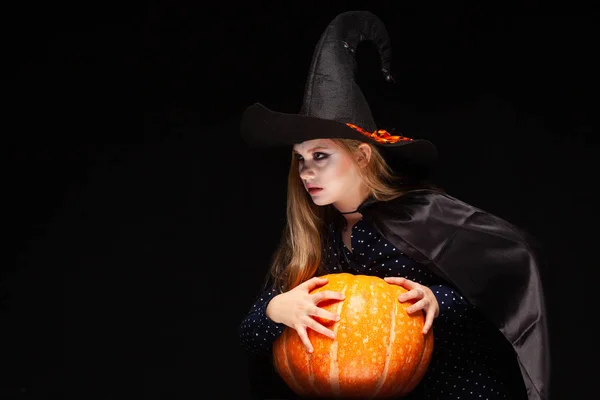 Bruja de Halloween con calabaza sobre fondo negro. Hermosa joven sorprendida mujer en sombrero de brujas y traje de calabaza celebración. Amplia fiesta de Halloween diseño de arte. Copia y pega. Concepto de bruja. Araña —  Fotos de Stock