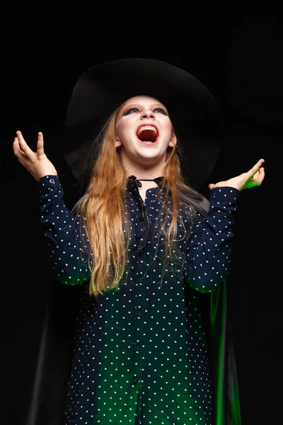 Bruxa de Halloween sobre um pote de líquido brilhante verde evoca as mãos no fundo preto. Linda jovem mulher surpreso em chapéu de bruxas e traje. Amplo design de arte de festa de Halloween. Copiar e colar. Bruxa. — Fotografia de Stock