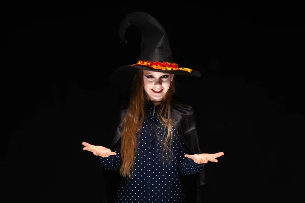 Sorcière d'Halloween sur fond noir. Belle jeune femme surprise en chapeau et costume de sorcières. Design d'art de fête Halloween large. Copier-coller. Le concept d'échelles, offre de choisir des cadeaux, placer des articles — Photo