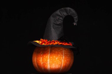 Cadılar Bayramı, kutlama. Güzel büyük turuncu balkabağının üzerinde örümcekler olan siyah cadı şapkası. Tasarım. Cadılar Bayramı sembolü kavramı. Yalıtılmış siyah arka plan.