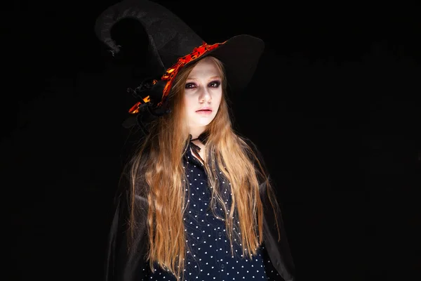 Halloween. Witch with a spider on his hat on black background. Beautiful young surprised woman in witches hat and costume holding. Wide Halloween party art design. Copy-paste. Witch craft concept.