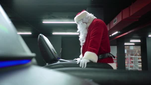 Санта Клаус тренируется в спортзале на Рождество. Санта Клаус бегает на беговой дорожке в фитнес-клубе — стоковое видео
