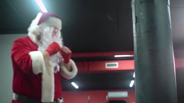 Santa Claus Fighter kickbox Con vendajes rojos boxeador golpeando un enorme saco de boxeo en un estudio de boxeo. boxeador de Santa Claus entrenamiento duro . — Vídeos de Stock