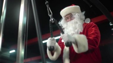 Noel günü spor salonunda Noel Baba eğitimi. Noel Baba trisepslerde egzersiz yapıyor..