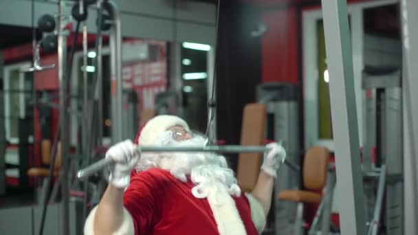 サンタクロースはクリスマスの日にジムでトレーニングをします。運動機械. — ストック動画