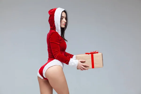 Weihnachten. Sport-Fitness-Mädchen im roten sexy Weihnachtsmann-Kostüm mit einer Geschenkschachtel, die mit einer roten Schleife mit Schleife gebunden ist. isoliert auf grauem Hintergrund. — Stockfoto