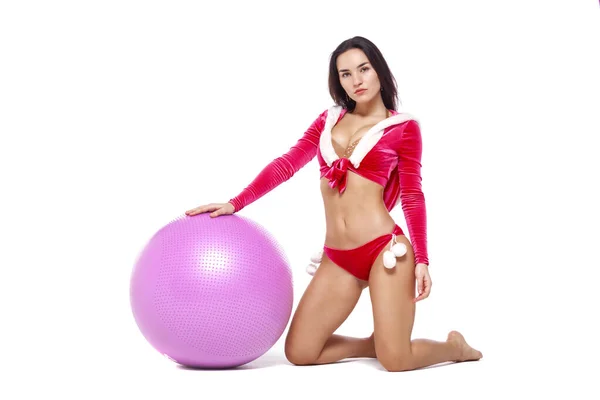 Kerstmis. Sport fitness meisje in rood sexy Kerstman kostuum zit op een fitness bal. Geïsoleerd op witte achtergrond. — Stockfoto