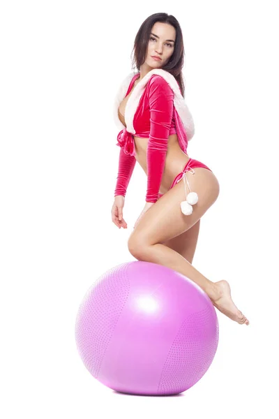 Kerstmis. Sport fitness meisje in rood sexy Kerstman kostuum staat op het fitness bal. Geïsoleerd op witte achtergrond. — Stockfoto