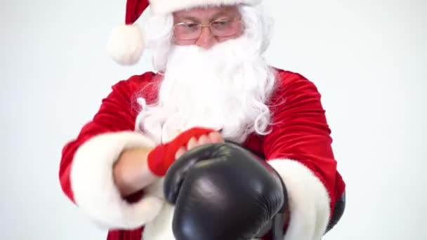 Julen. Santa Claus på en vit bakgrund bär svarta boxningshandskar och uppfyller stansar. Kickboxning, kämpe. Bär handskar på röda bandage. — Stockvideo