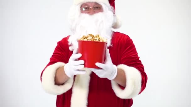 Santa Claus sobre un fondo blanco con un cubo rojo de palomitas de maíz. Come palomitas y ve una película, ofrece palomitas de maíz . — Vídeos de Stock