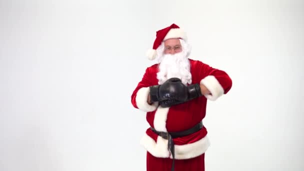 Christmas. Santa Claus on a white background wears black boxing gloves and fulfills punches. Kickboxing, fighter. He takes off his gloves and throws them. The training or battle is over. — ストック動画