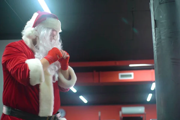 Kickbox Santa Claus Fighter Z Red Bandages bokser uderzając ogromny worek bokserski w studio bokserskim. Santa Claus bokser trening ciężko. — Zdjęcie stockowe
