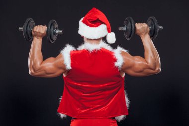 Seksi Noel Baba. Vücut geliştirici genç yakışıklı Noel Baba 'nın gülümseyişi yılbaşı arifesinde ve Noel tatilinin kara arka planında bir dambıl tutuyor. Arkadan manzara..