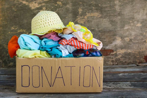 Donation box with summer clothes on the old wooden background.