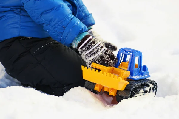 Winter. Child playing in the snow. Image of a child sitting on white snow and playing with a toy excavator.