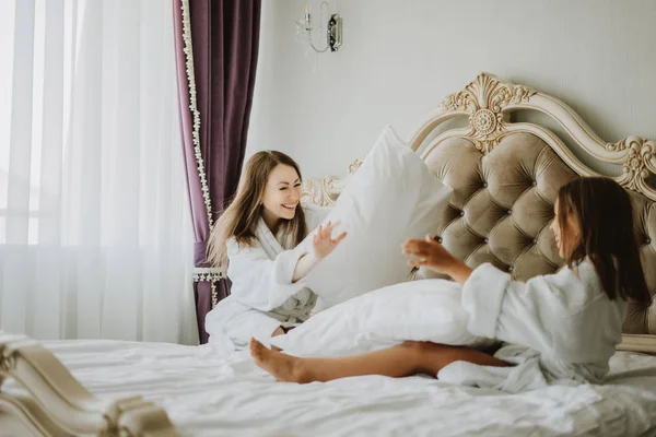 Mom and daughter are fighting pillows on the bed, pillow fight