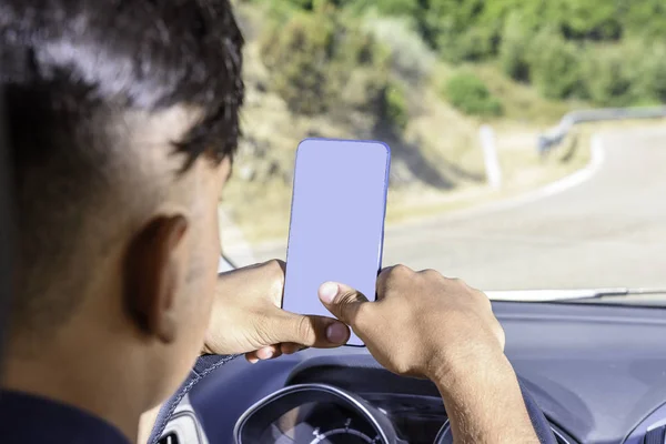Młody kierowca, za pomocą smartfona, na drodze w samochodzie. — Zdjęcie stockowe