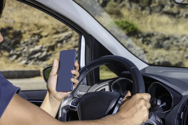 Jonge bestuurder, met behulp van smartphone, op de weg in de auto. — Stockfoto