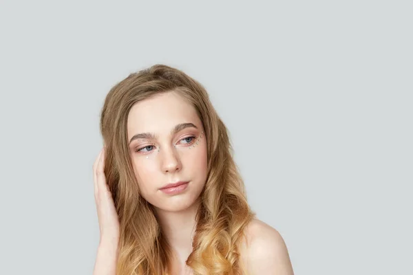 Una joven con un hermoso maquillaje se ve a un lado y endereza su cabello . —  Fotos de Stock